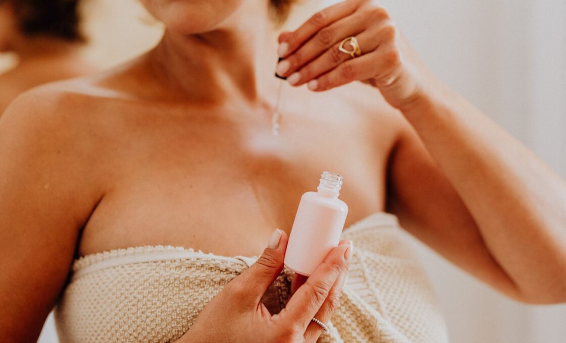 Woman applying a skincare serum in front of a bathroom mirror