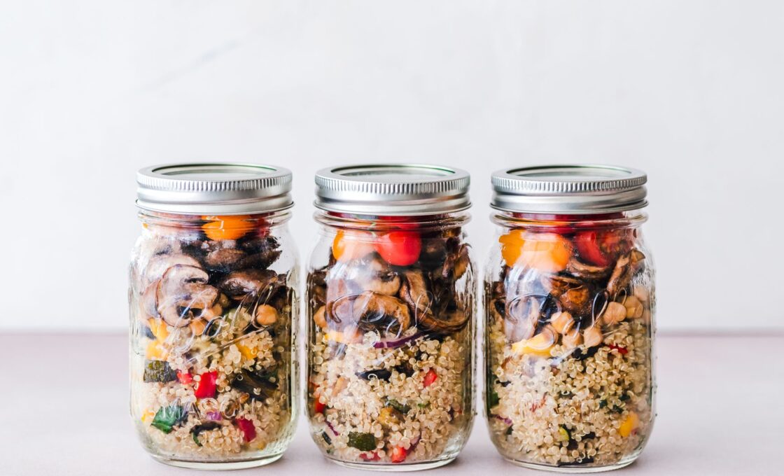 Glass containers of prepped grains, vegetables, and greens on a kitchen counter