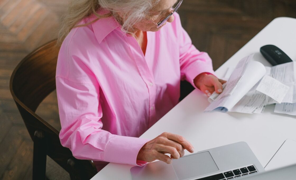 Woman at a kitchen table reviewing health savings account statements on a laptop