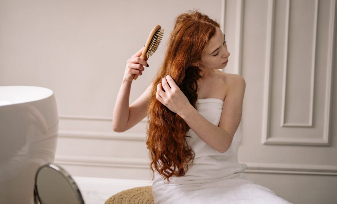 Woman combing out sun-damaged hair in front of a bathroom mirror