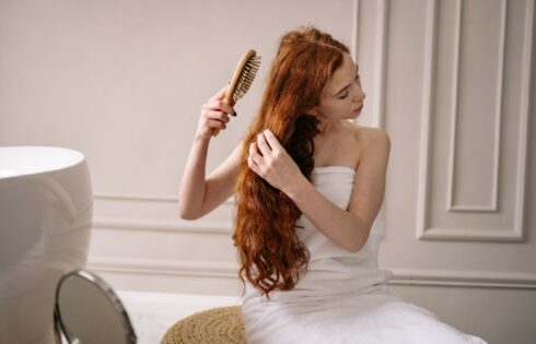 Woman combing out sun-damaged hair in front of a bathroom mirror