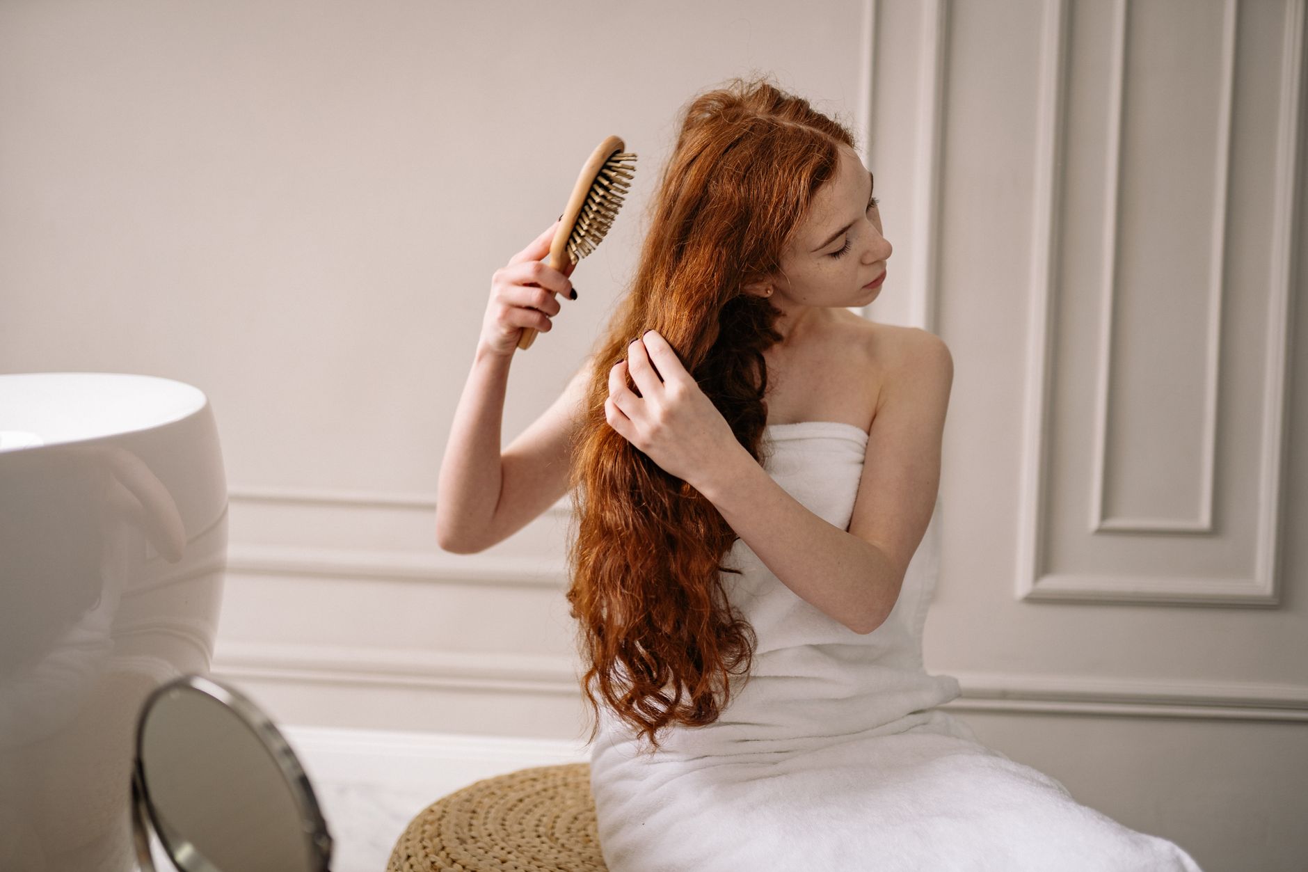 Woman combing out sun-damaged hair in front of a bathroom mirror