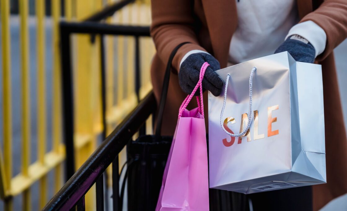 Woman carrying shopping bags while comparing holiday sale prices before Black Friday