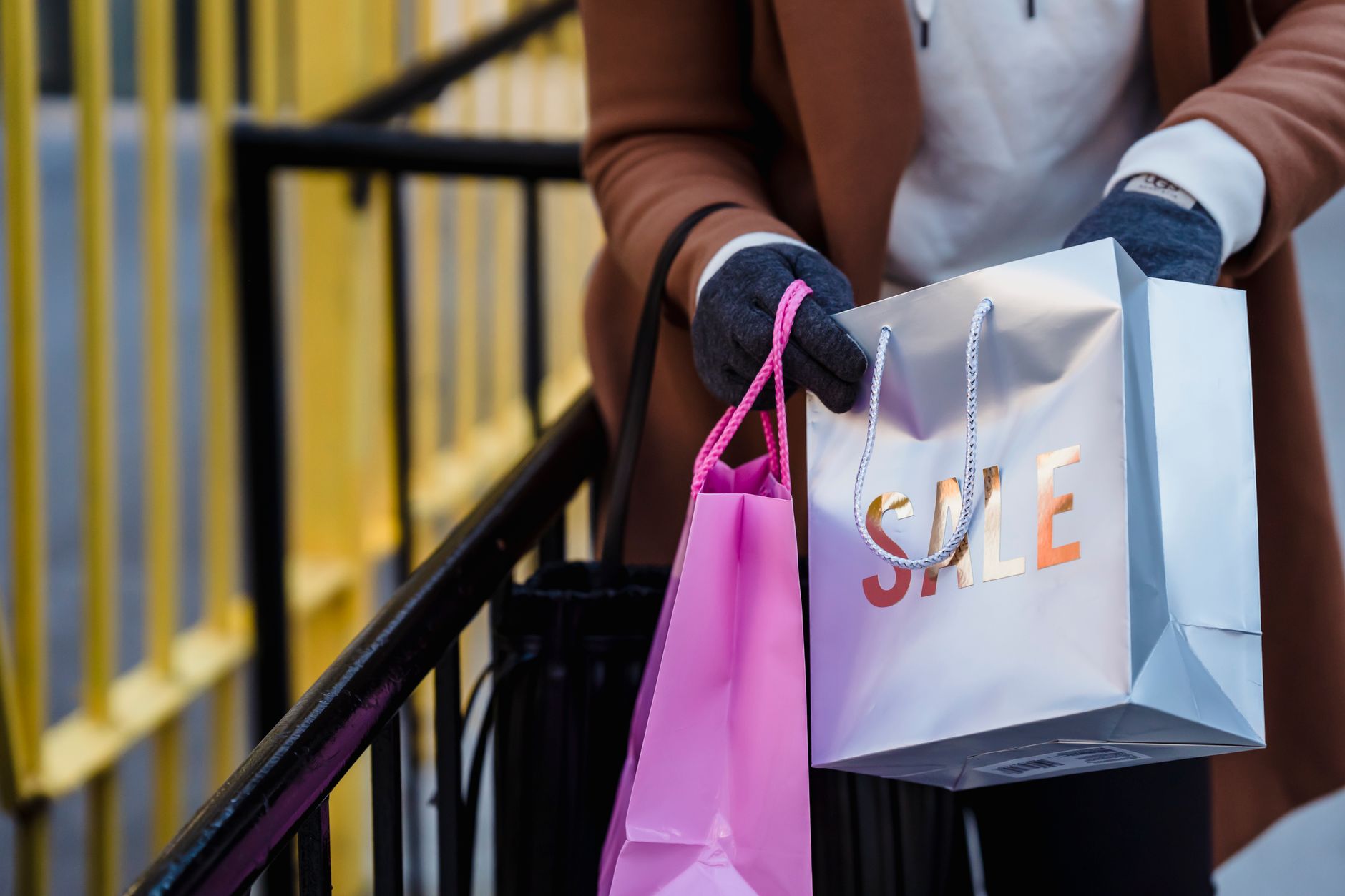 Woman carrying shopping bags while comparing holiday sale prices before Black Friday