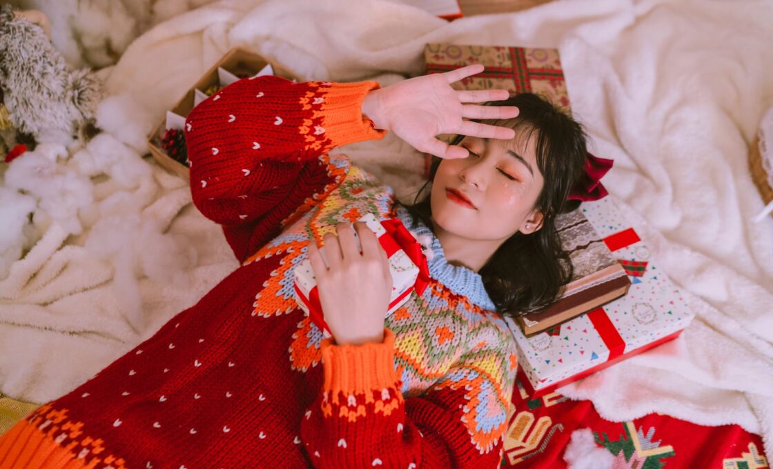 Woman in a festive sweater surrounded by wrapped holiday gifts, illustrating beauty advent calendar season