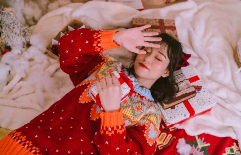 Woman in a festive sweater surrounded by wrapped holiday gifts, illustrating beauty advent calendar season