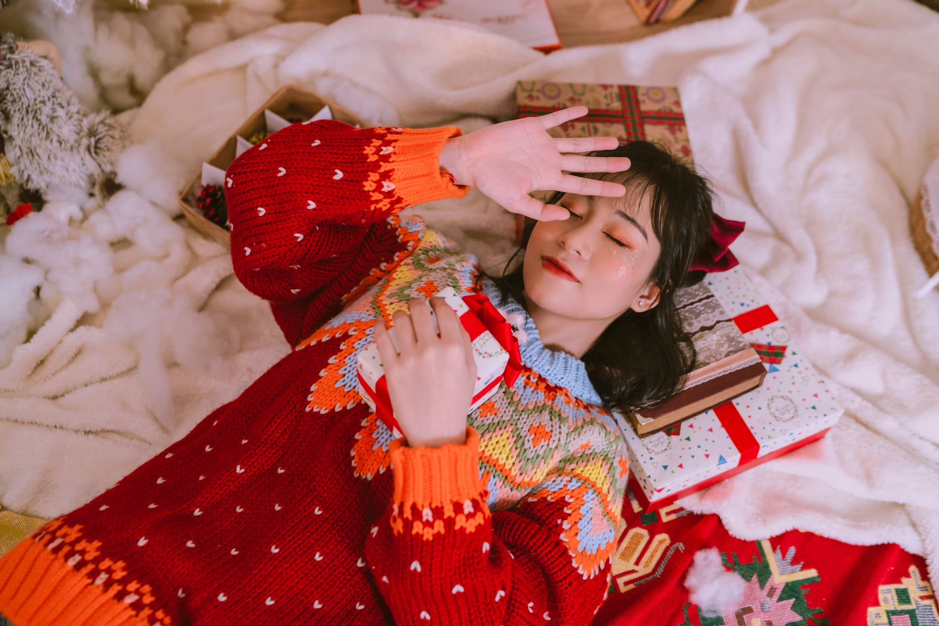 Woman in a festive sweater surrounded by wrapped holiday gifts, illustrating beauty advent calendar season