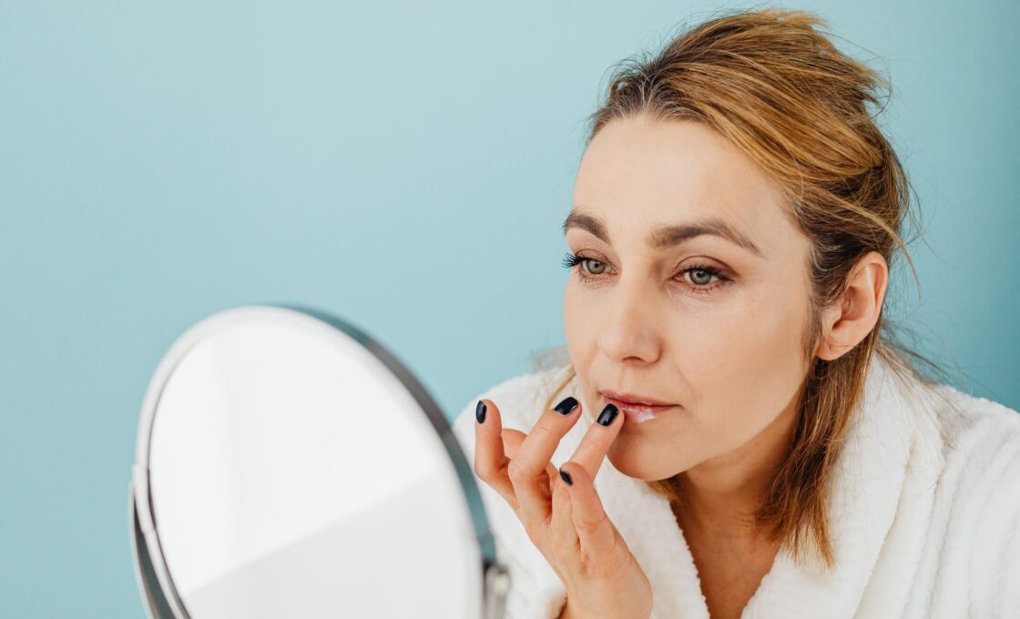 Woman in a bathrobe applying lip balm to chapped lips in a mirror