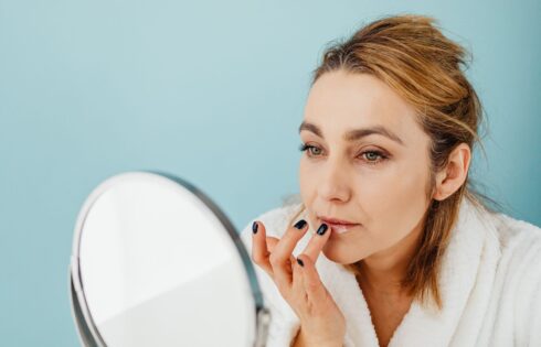 Woman in a bathrobe applying lip balm to chapped lips in a mirror