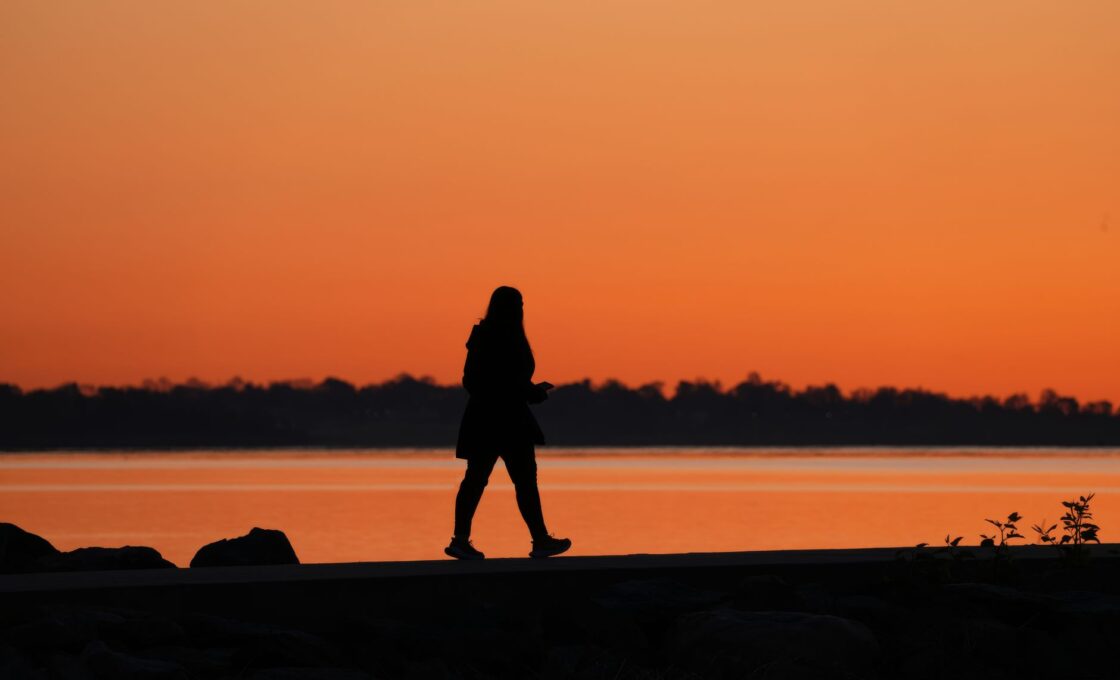 Silhouette of a woman walking at sunset as evenings get darker after daylight saving time ends