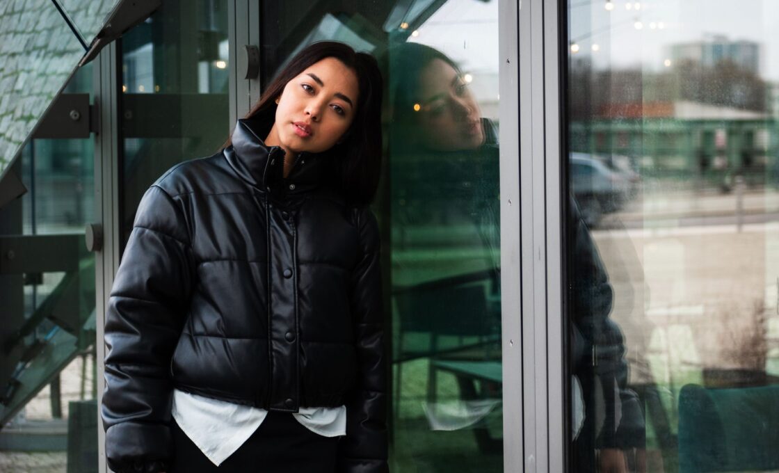 Woman in a black winter jacket leaning against a glass wall, illustrating how to choose a warm down coat