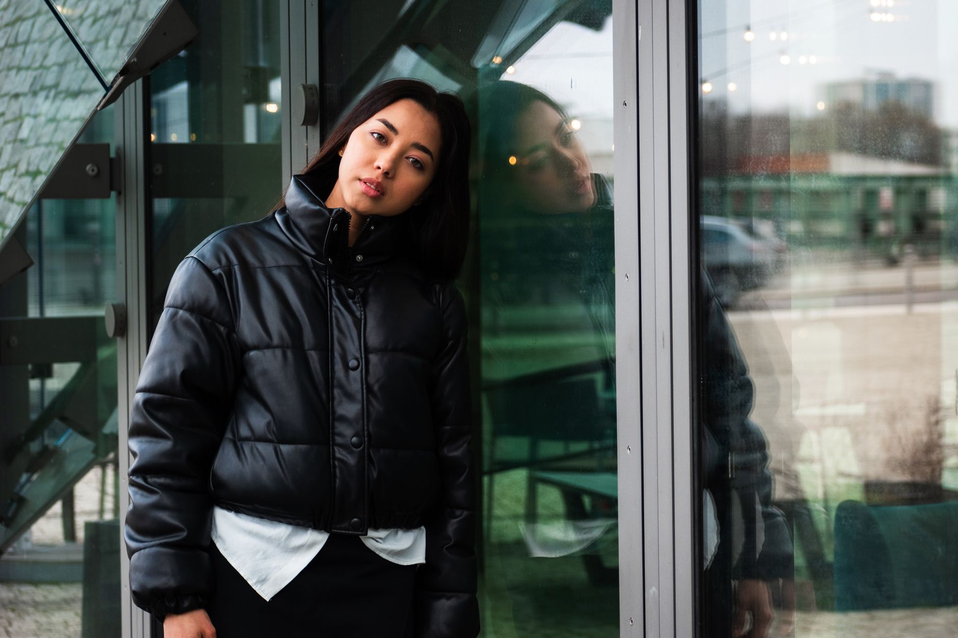 Woman in a black winter jacket leaning against a glass wall, illustrating how to choose a warm down coat