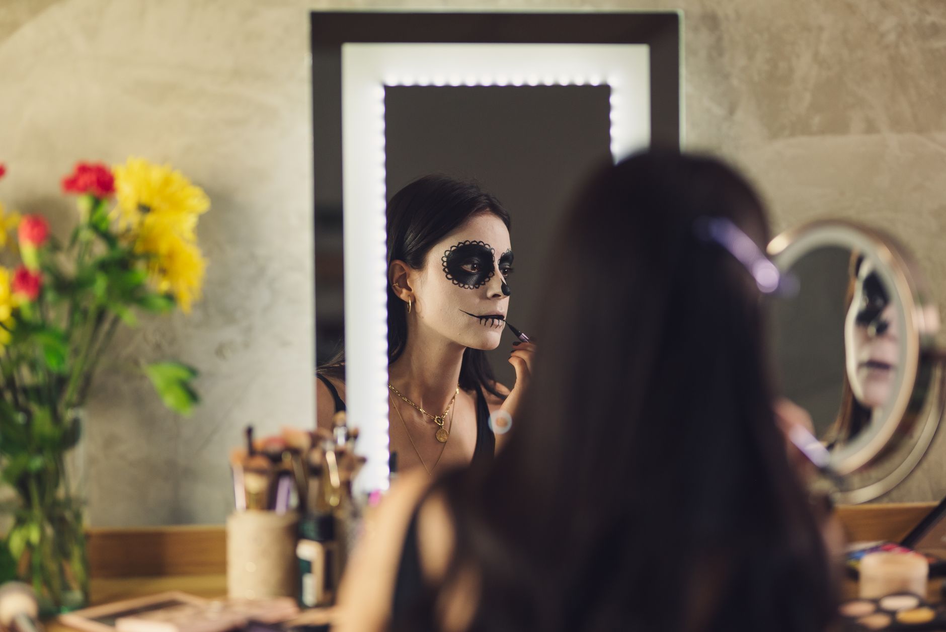 Woman applying skull face paint in front of a mirror, a reminder to keep costume makeup away from the eye area