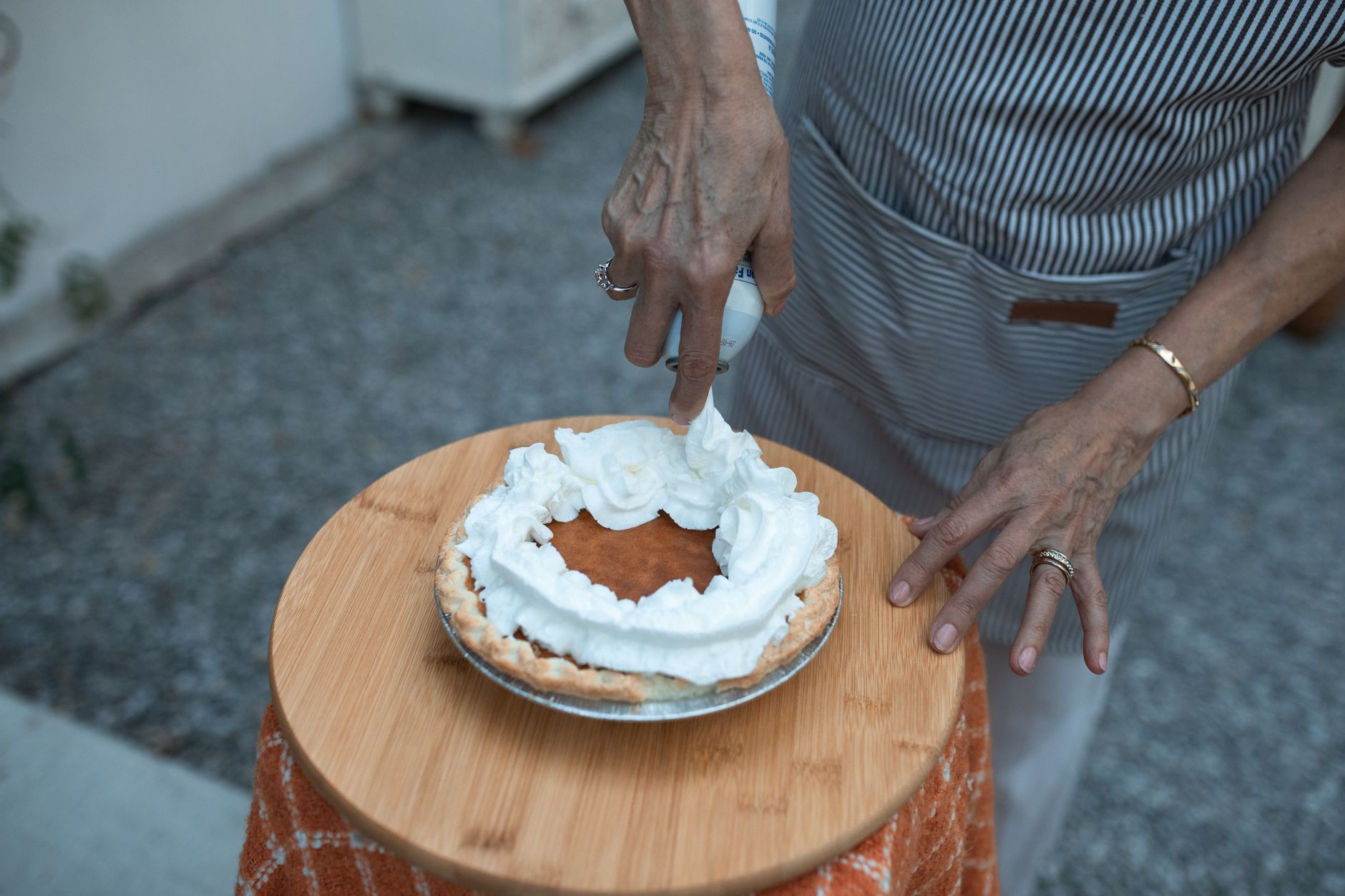 Hands adding whipped cream to a slice-ready homemade pumpkin pie for Thanksgiving