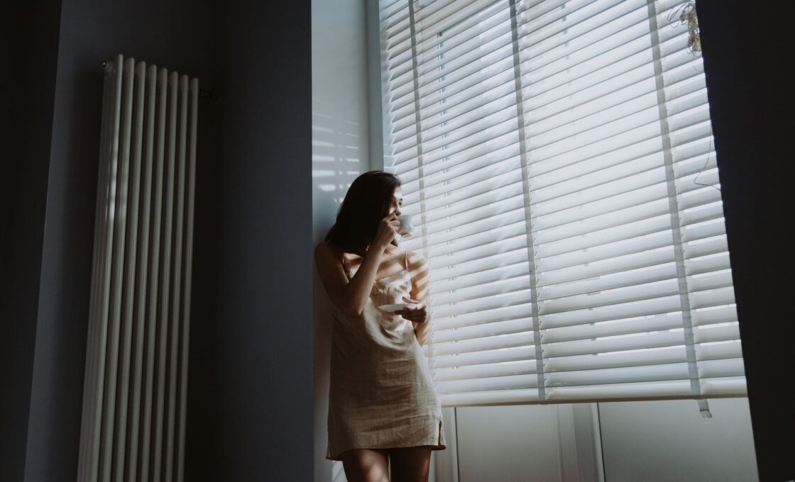 Woman drinking coffee by a bright window on a fall morning, the first-hour light window for a light therapy lamp