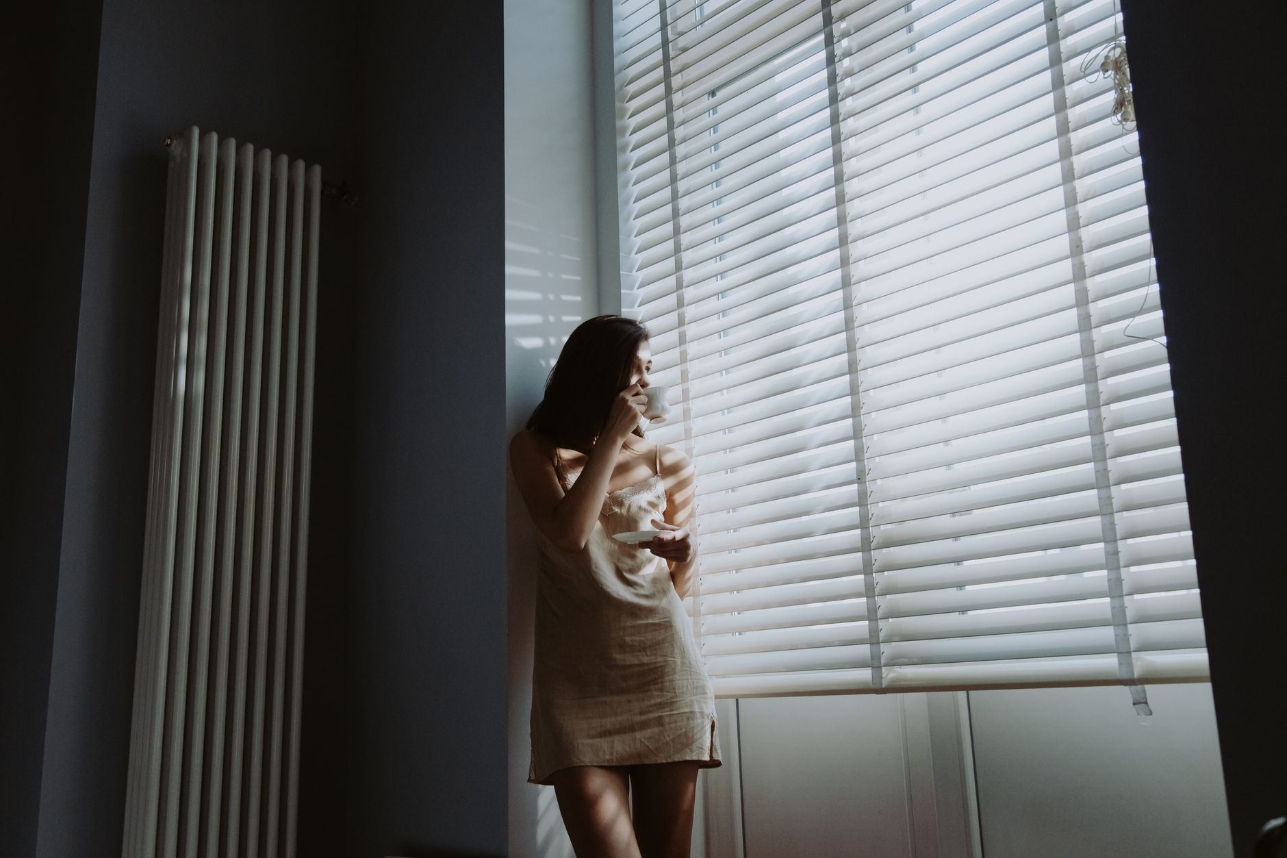 Woman drinking coffee by a bright window on a fall morning, the first-hour light window for a light therapy lamp