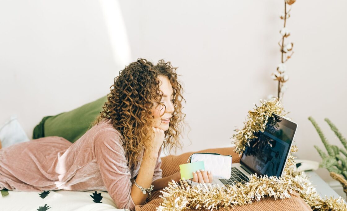 Woman holiday shopping online on a laptop decorated with Christmas tinsel, comparing gift card options