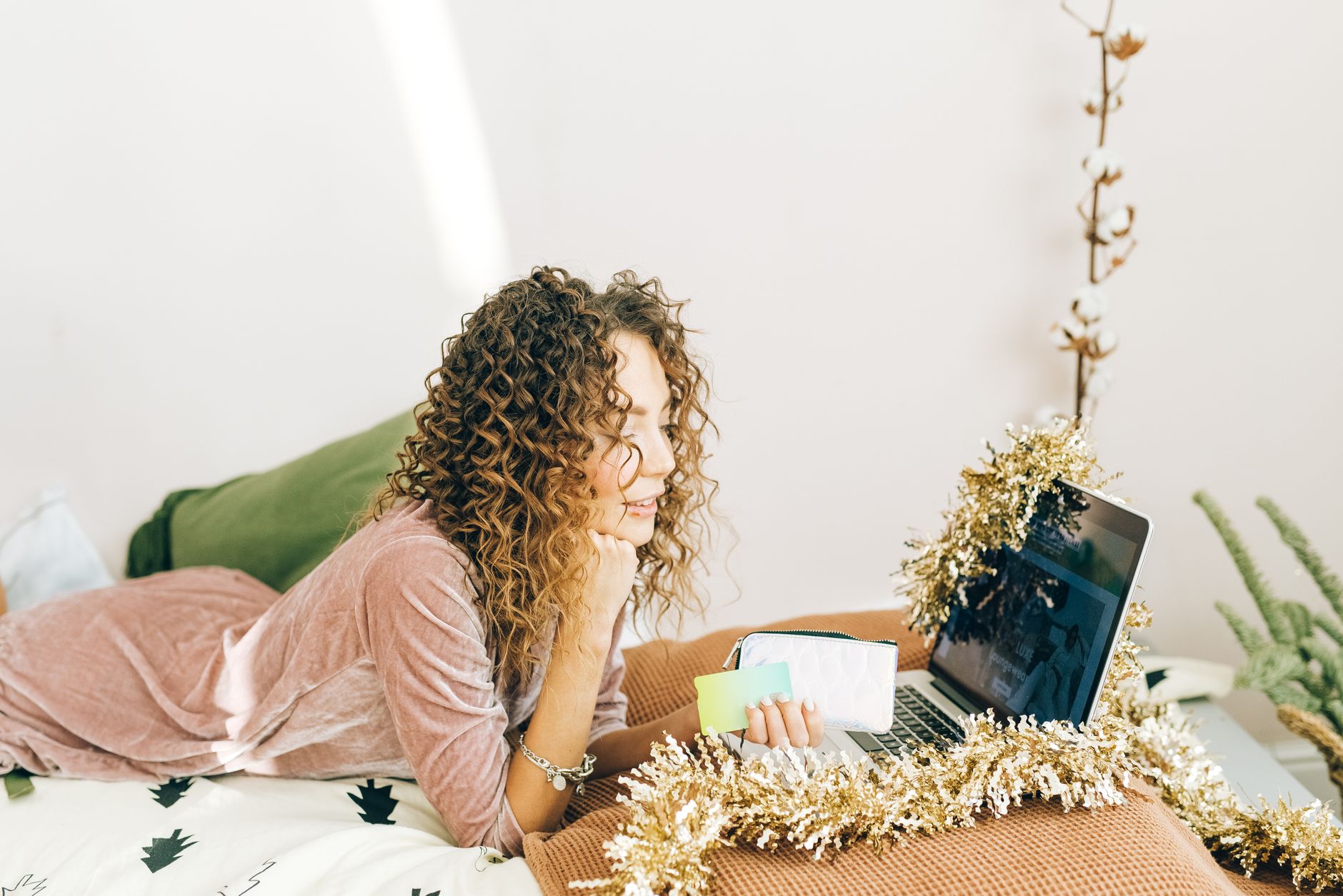 Woman holiday shopping online on a laptop decorated with Christmas tinsel, comparing gift card options